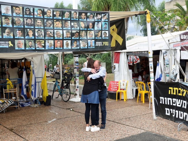 Personas se abrazan junto a una pancarta con fotos de rehenes en la "Plaza de los Rehenes". Foto: REUTERS/Ronen Zvulun