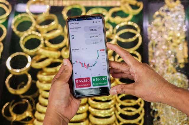 A woman uses the Gold Now app, an online gold trading and savings application developed by Thailand's gold dealer Hua Seng Heng, on her mobile phone as she checks gold price, in Bangkok, Thailand, September 22, 2025. REUTERS/Chalinee Thirasupa
