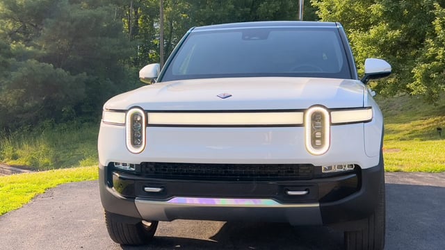 A white Rivian R1S in the late afternoon sun, seen head-on