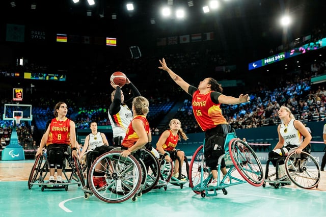 Zwei Rollstuhlbasketball-Teams stehen sich auf dem Feld gegenüber, eine Person setzt zum Wurf an