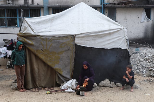 A Palestinian woman builds a fire as children look towards it while beside a tent, after U.S. President Donald Trump announced that Israel and Hamas agreed on the first phase of a Gaza ceasefire, in Khan Younis in the southern Gaza Strip October 9, 2025. REUTERS/Ramadan Abed