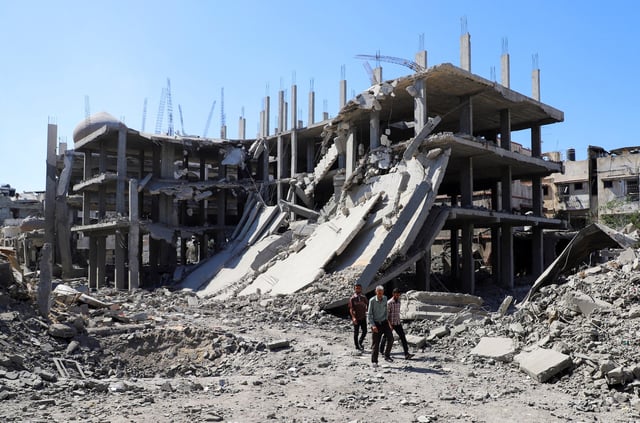 Palestinians walk past a destroyed building, as they inspect the damage in the aftermath of Israeli operation at Sabra neighbourhood in Gaza City, October 8, 2025. REUTERS/Ebrahim Hajjaj     TPX IMAGES OF THE DAY