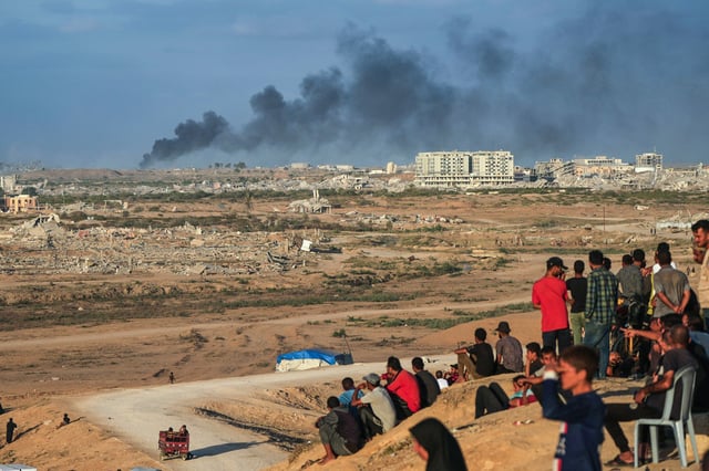 Displaced Palestinians watch smoke rise after Israeli military strikes as they gather on the coastal road near Wadi Gaza, in the central Gaza Stripnon Oct. 9, 2025.