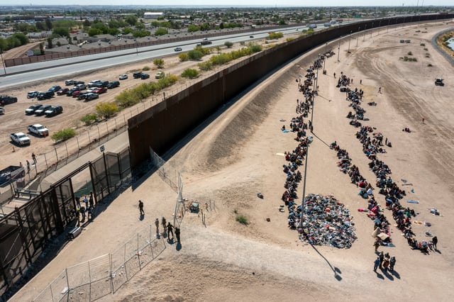 Migrants form lines outside the border fence waiting for transportation to a U.S. Border Patrol facility in El Paso, Texas.