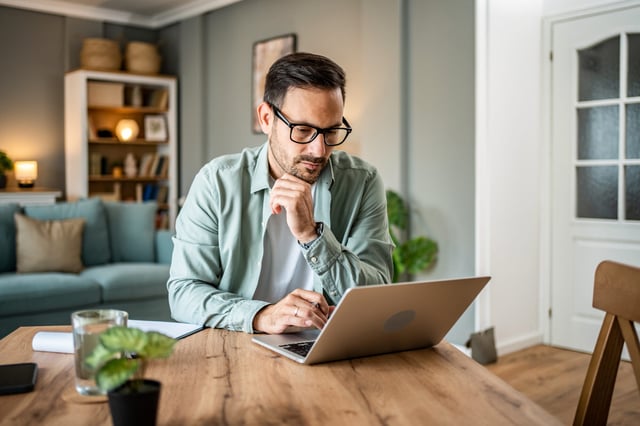 Man sitting at dining room table looking at laptop.