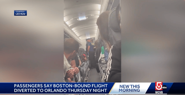 Screenshot shows an airline crew escorting a passenger down the aisle as other passengers look toward the back of the aircraft where an incident took place.