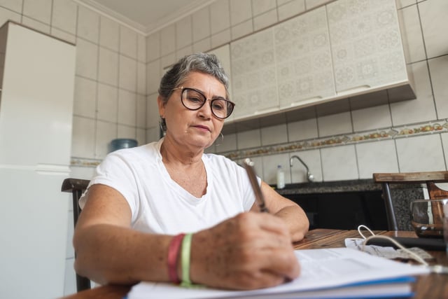 Older woman sitting at kitchen table filling out forms