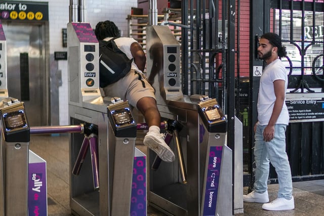 A man goes over a subway turnstile without paying the MTA fare as other wait for him to open the door at a subway station in middle Manhattan on June 5, 2023 in New York City.