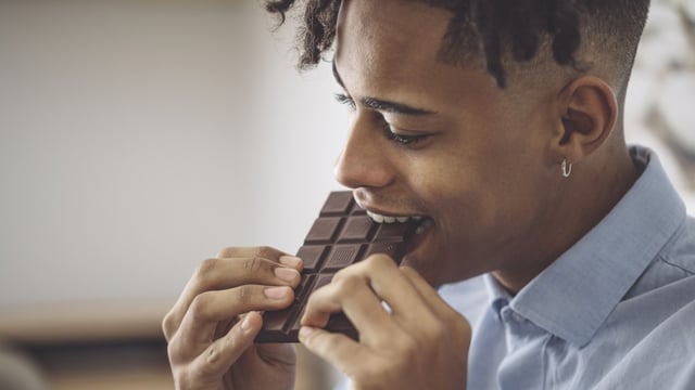 A man wearing a blue shirt taking a bite out of a whole block of milk chocolate