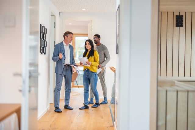 An adult male real estate agent gives an apartment tour to a young diverse couple.
