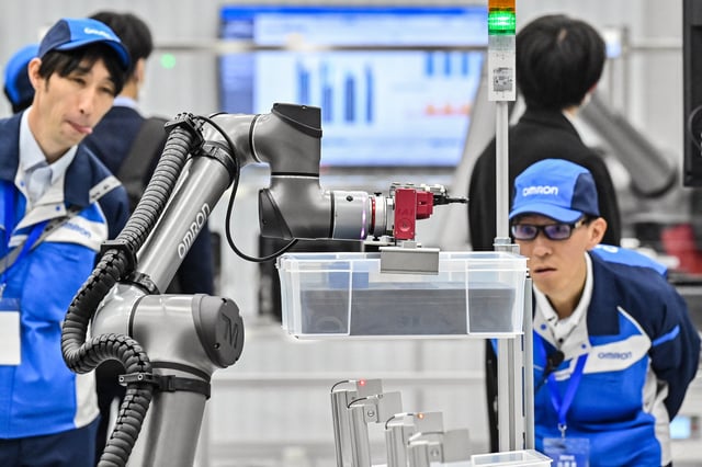 Photo of two employees watching a robotic arm moves items on an assembly line.