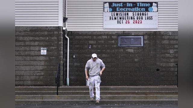 A painter passes a "Lewiston Strong!" sign displayed outside the Just-In-Time bowling alley, one of the sites of the Lewiston shootings, while taking a break from renovating following the incident.