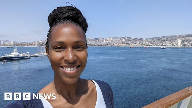 Brandee Lake smiling at the camera in a selfie, her braids are worn in a high bun and she is stood by a sea port.