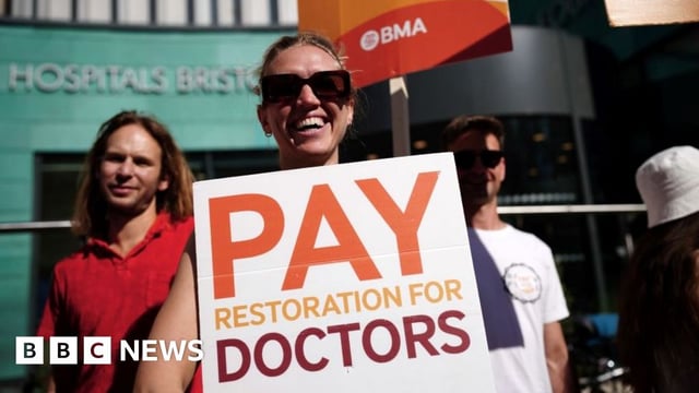 Photo of a striking doctor in glasses holding a placard, which reads 'pay restoration for doctors'