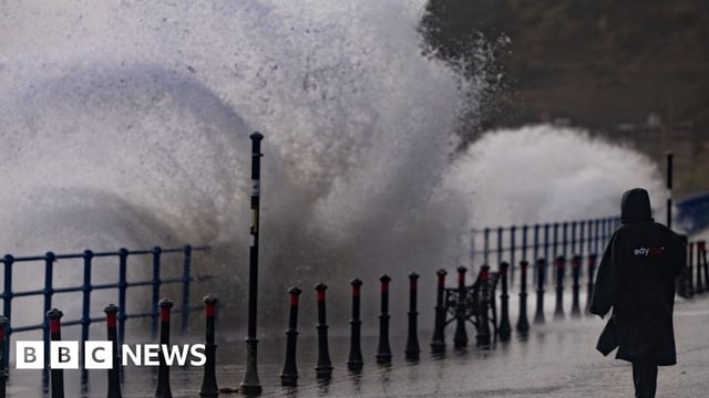 A woman stands on a seaside promenade as waves crash over