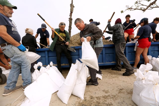 Residents, with the help of lifeguards, collect bags of sand in preparations for upcoming storm in Long Beach, California, on Saturday.
