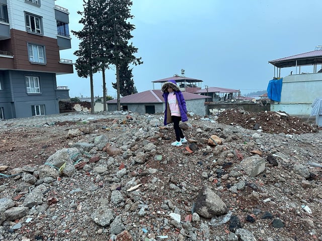 Sengul Karabas, now 7, stands on what remains of their former home in Islahiye. She lost her mother and brother when the building collapsed in the earthquake.