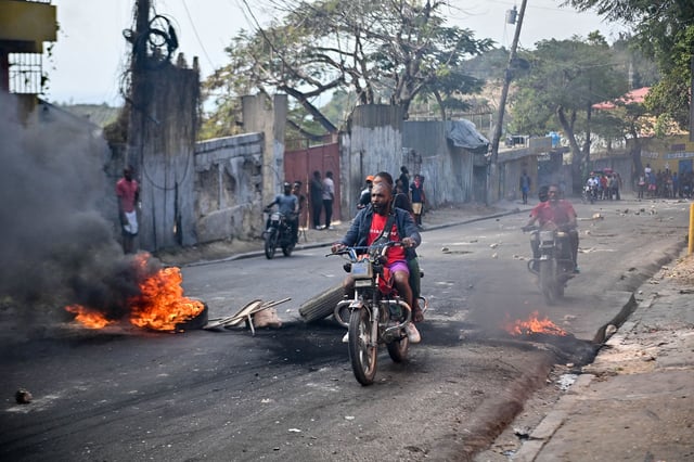 People ride motorbikes past burning tires during a demonstration calling for the resignation of Prime Minister Ariel Henry, in Port-au-Prince, Haiti, on February 6, 2024. Haiti's government on February 5, 2024 announced a crackdown on the para-military and environtmental agency Protected Areas Security Brigade (BSAP) whose heavily armed agents have gained power recently and have been blamed for violent clashes with police last week. (Photo by Richard PIERRIN / AFP) (Photo by RICHARD PIERRIN/AFP via Getty Images)