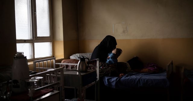 An unidentifiable woman holds her baby son on a hospital bed