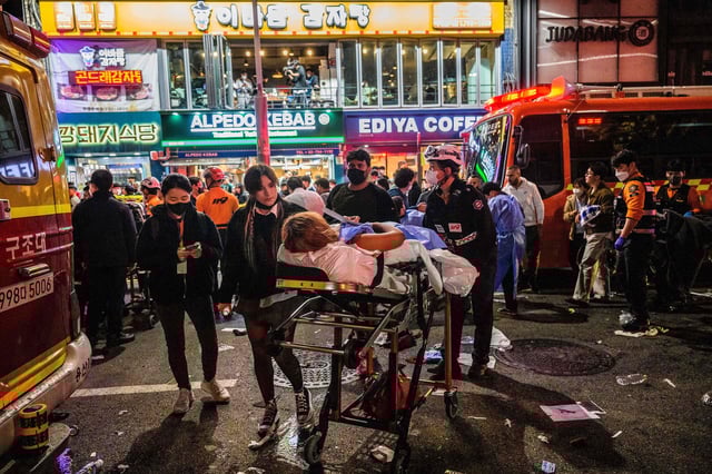 In this photo taken early on October 30, 2022, rescue workers help a person (C) on a stretcher after a Halloween crowd crush that took place in a nearby alleyway in the popular district of Itaewon in Seoul. - Families of the Itaewon victims want answers about why authorities failed to prevent the catastrophe despite clear warning signs, with some families forming a group "to understand what really happened and to hold those officials responsible." But the internet interpreted their efforts to organise as an attack on the government, with right-wing trolls launching a coordinated counter-attack, accusing the families of being profiteers out for compensation, or anti-government forces. (Photo by Anthony WALLACE / AFP) / To go with AFP story SKorea-internet-disinformation-accident,FOCUS by SHIM Kyu-Seok (Photo by ANTHONY WALLACE/AFP via Getty Images)