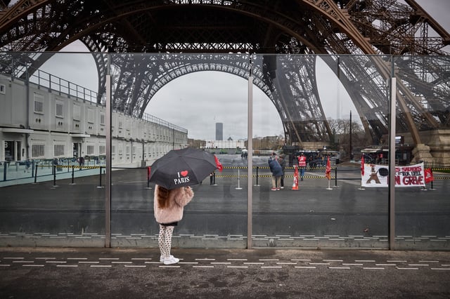 A pedestrian with an umbrella reading "I Love Paris" looks on next to the Eiffel Tower and a displayed banner reading "employees of the Eiffel Tower on strike" in Paris on Monday. Unions of the operating company of the Eiffel Tower, the CGT and Force Ouvriere say the city, which owns 99 percent of the tower, has underestimated costs and overestimated revenues, whilst also hinting to the threat of a strike during the Olympic Games, held in Paris from July 26 to August 11.