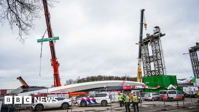 Emergency services on the scene of the bridge collapse at a construction site. Cranes and a partially constructed bridge are visible behind.