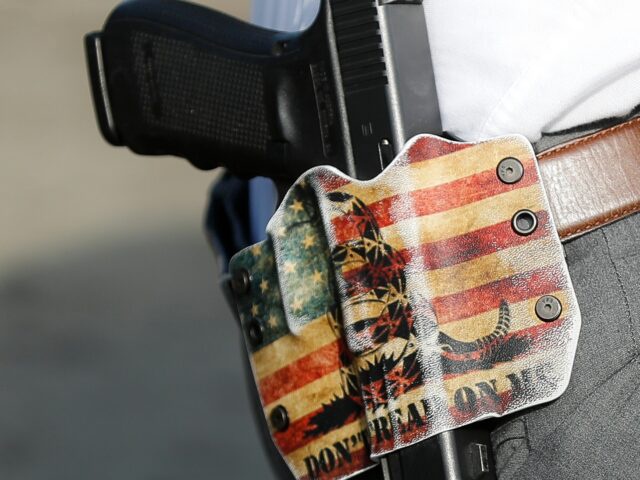 A Dayton Police detective wears his sidearm in a holster bearing the phrase "DON'T TREAD ON ME" as he performs a grid search beside a makeshift memorial for the slain and injured in the Oregon District after a mass shooting that occurred early Sunday morning, Tuesday, Aug. 6, 2019, in Dayton. Facing pressure to take action after the latest mass shooting in the U.S., Ohio's Republican governor urged the GOP-led state Legislature Tuesday to pass laws requiring background checks for nearly all gun sales and allowing courts to restrict firearms access for people perceived as threats. (AP Photo/John Minchillo)