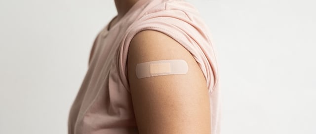 Asian woman shows plaster on her shoulder after being vaccinated against Covid-19. Coronavirus vaccination campaign concept.
