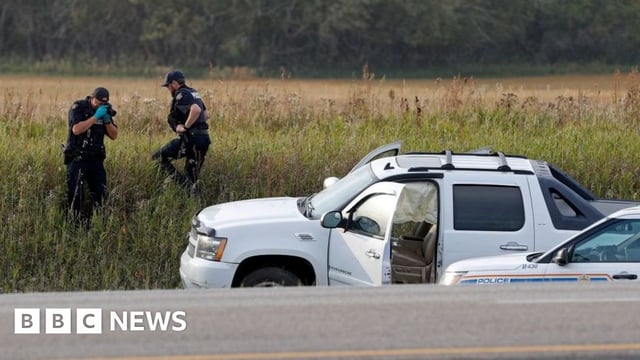 A Royal Canadian Mounted Police officer takes a pictures of police vehicles next to a pickup truck at the scene where suspect Myles Sanderson was arrested,