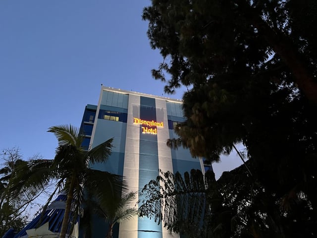 An exterior view of the Disneyland Hotel at dusk with an illuminated sign, surrounded by tropical foliage, Anaheim, Calif., Jan. 3, 2024. 