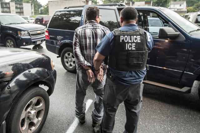 A suspect is escorted by an ICE agent for transportation to Baltimore.