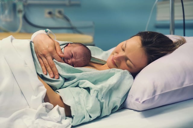 A mom holds a newborn baby while lying in a hospital bed