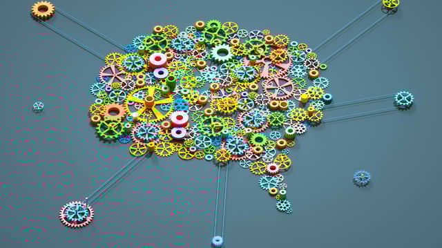 Digital generated image of multi coloured gear wheels connected together in shape of brain on grey background.