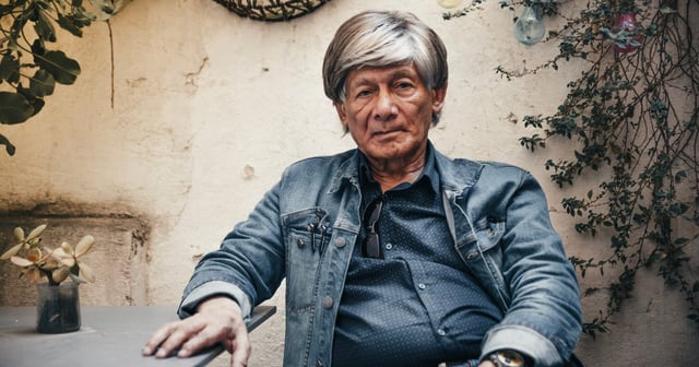 Charles Sobhraj sitting at a table looking at the camera.