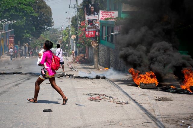 A woman carrying a child runs away from gunshots in Port-au-Prince, Haiti, on March 20, 2024. 