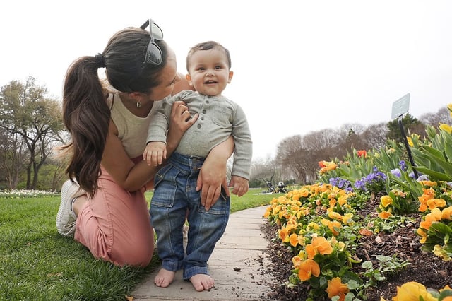 Francisco Castillo, age 1, smiles as his mother, Liliana Mendoza, helps him stand as they enjoy a warm day at the Dallas Arboretum and Botanical Garden in Dallas, Feb. 27, 2024. 