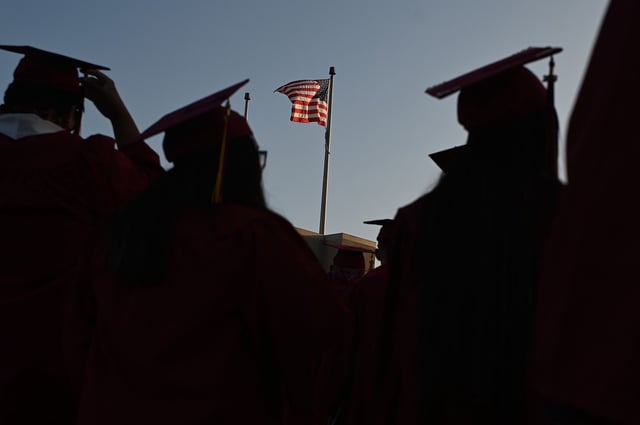 A US flag flies above a building as students earning degrees at Pasadena City College participate in the graduation ceremony, June 14, 2019, in Pasadena, California. - With 45 million borrowers owing $1.5 trillion, the student debt crisis in the United States has exploded in recent years and has become a key electoral issue in the run-up to the 2020 presidential elections. "Somebody who graduates from a public university this year is expected to have over $35,000 in student loan debt on average," said Cody Hounanian, program director of Student Debt Crisis, a California NGO that assists students and is fighting for reforms.