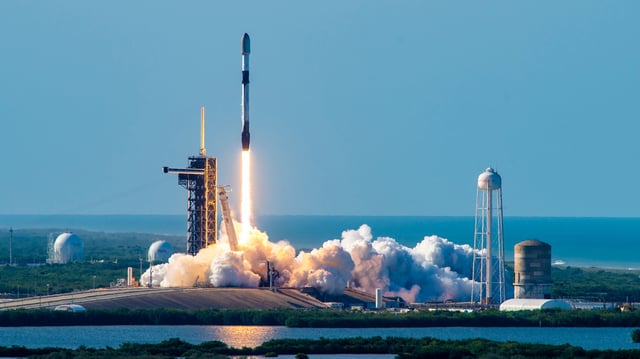 a black-and-white spacex falcon 9 rocket launches into a blue sky.