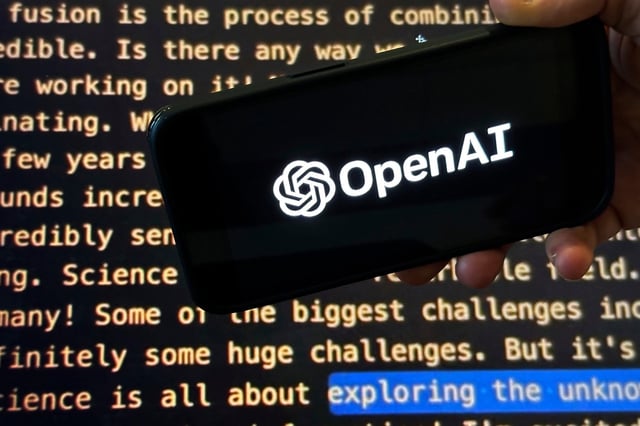 The OpenAI logo appears on a mobile phone in front of a screen showing a portion of the company website, Nov. 21, 2023. Photo: AP