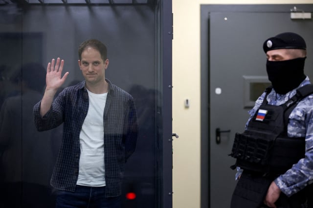 Wall Street Journal reporter Evan Gershkovich waves behind a glass wall of an enclosure for defendants as he attends a court hearing in Moscow, Russia, on April 23.