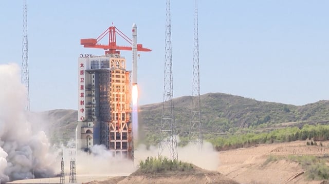 a large white rocket lifts off during the day with mountains visible behind it