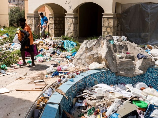 Asylum seekers walk amidst waste at the Ayios Nikolaos apartment complex, in Chloraka, a village of 7000 people located on the outskirts of Paphos, on August 22, 2023. Cypriot authorities have started removing around 600 asylum seekers from the condemned apartment complex near the resort of Paphos after protests by residents. European Union member Cyprus argues it is a "frontline country" on the Mediterranean migrant route, with asylum-seekers accounting for five percent of the 915,000 people living in government-held areas of the island - the highest proportion in the bloc. (Photo by Iakovos Hatzistavrou / AFP) (Photo by IAKOVOS HATZISTAVROU/AFP via Getty Images)