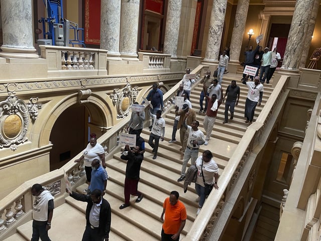 Dozens of protesters descend a staircase in the Minnesota State Capitol building in St. Paul, Minn., Friday, May 17, 2024, while holding signs and pushing for a law that would require ride-hailing companies – including Uber and Lyft -- to increase pay for drivers in the state. Uber and Lyft have said they will leave the state if Minnesota lawmakers pass legislation requiring the companies to raise driver pay by more than the companies want to.