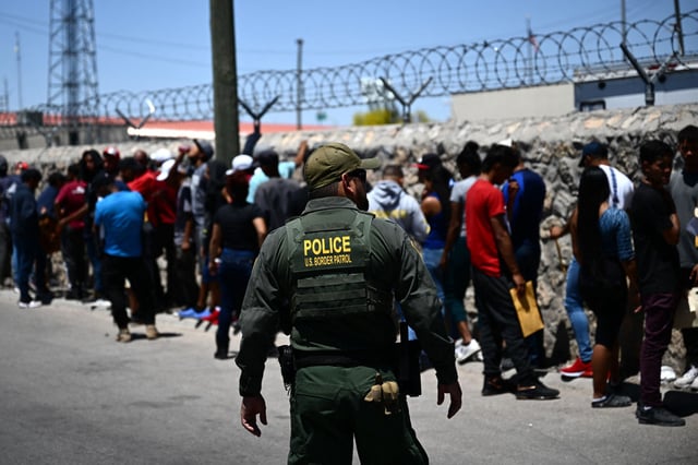 A Border Patrol agent walks along a line of migrants near the Paso del Norte Port of Entry in El Paso, Texas, on May 9, 2023.