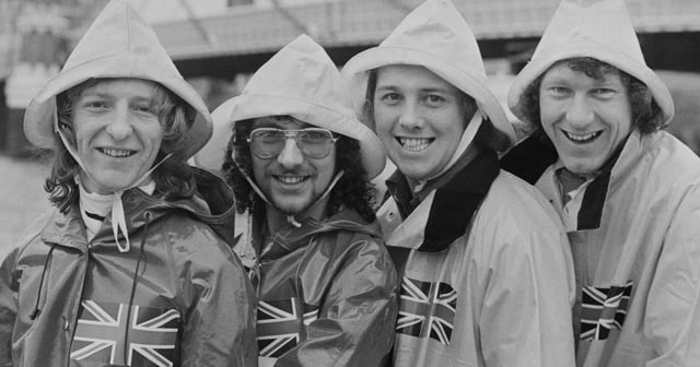 Colin Gibb, Alan Barton, Steve Scholey and Nigel Scott in raincoats smiling into camera