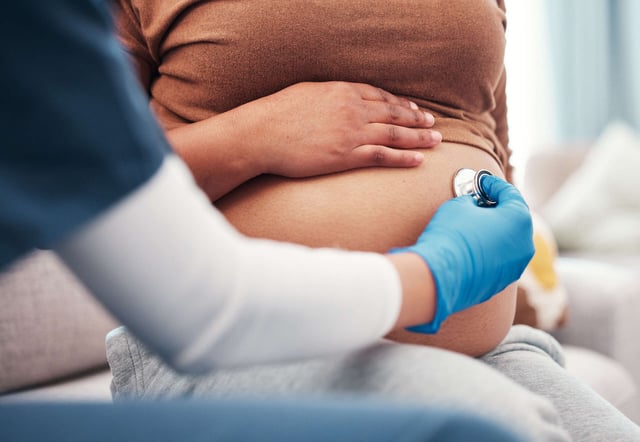A health care worker performs a check-up with a stethoscope on a pregnant woman