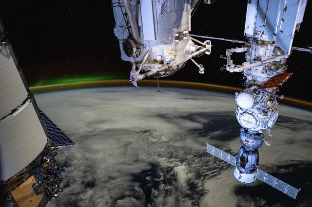 A dim aurora and an atmospheric glow crown Earth's horizon in this photograph from the International Space Station as it orbited 266 miles above a cloudy Indian Ocean southwest of Australia. In the foreground, from left, are a portion of Northrop Grumman's Cygnus space freighter, the Rassvet module, and the Soyuz MS-25 crew ship docked to the Prichal docking module which is itself mated to the Nauka science module. Credit: NASA