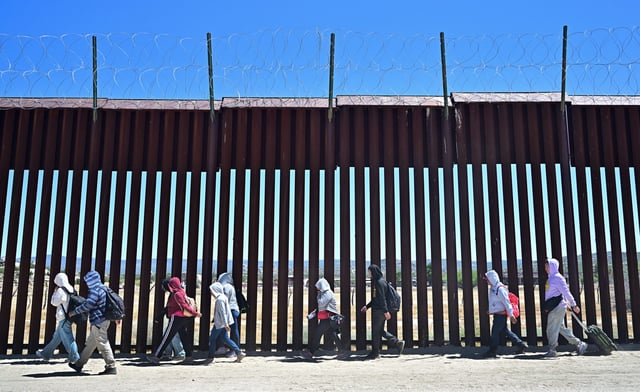 Migrants walk on the US side of the border wall in Jacumba Hot Springs, California on June 5, 2024, after crossing from Mexico.