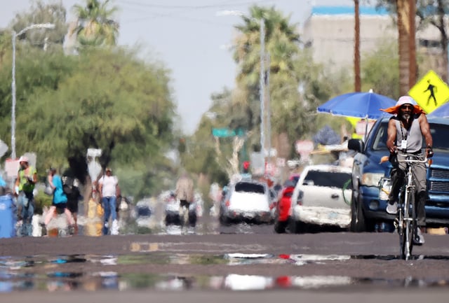 A person rides a bicycle as heat waves shimmer, causing visual distortion, as people walk in the 'The Zone', Phoenix's largest homeless encampment, amid the city's worst heat wave on record on July 25, 2023 in Phoenix, Arizona. Cities must plan to mitigate the effects of worsening temperatures in hotter, longer summer months.