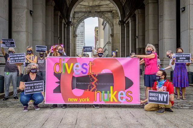 People stand behind a banner reading "Divest New York Nukes" during an outdoor demonstration